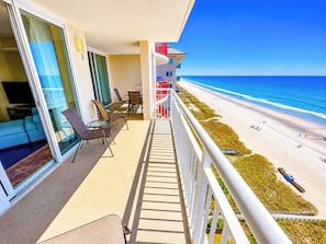 Un balcon avec vue sur la plage, un coin salon avec des chaises et une table.