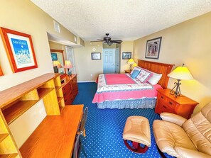 Una habitación de hotel con cama, escritorio, silla, armario y ventilador de techo.