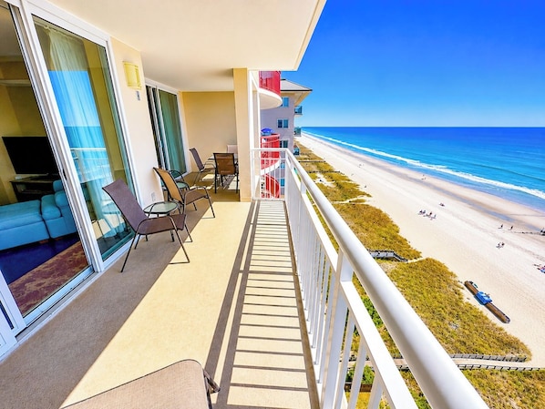 A balcony with a view of the beach, outdoor seating, and a pool area.