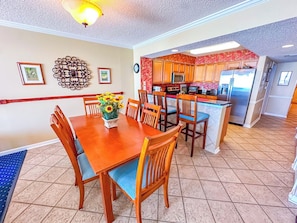A dining area with a wooden table and chairs, a kitchen with wooden cabinets and stainless steel appliances, and a decorative wall piece.