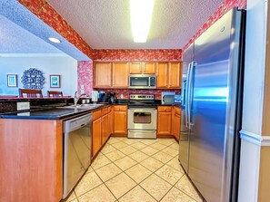 A kitchen with wooden cabinets, a stainless steel refrigerator, a microwave, and a stove. - South Shore Villas 1202 (North Myrtle Beach)