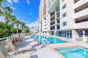 A swimming pool area with lounge chairs and a multi-story building with balconies.