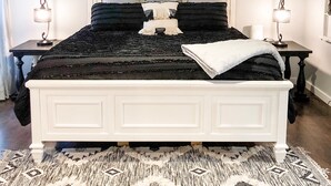 Une chambre avec un lit, deux tables de chevet, un ventilateur de plafond et un panneau mural sur lequel est écrit : « Restez un peu ».