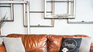 Un canapé en cuir marron agrémenté de coussins à motifs, un objet décoratif en verre posé sur une table en bois, et une œuvre d’art géométrique accrochée au mur.
