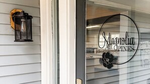 Une porte avec un panneau de verre sur lequel on peut lire « Magnolia Pines », et une lanterne décorative en métal fixée au mur.