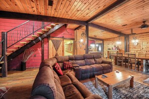 A cozy interior with a wooden ceiling, a red wall, a brown leather sofa, a dining area, and a staircase.