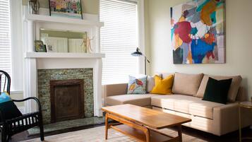 A living room with a beige sofa, a wooden coffee table, a fireplace, and a colorful abstract painting on the wall.