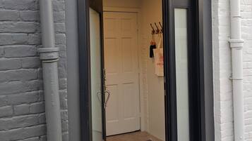 A building entrance with a black-framed door, a white door, and a colorful rug on the floor.