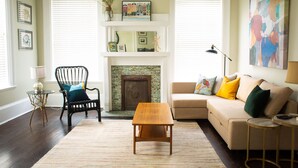 A living room with a fireplace, a sofa, a wooden coffee table, and a chair. - The Calliope, Historic Corner Apartment in the Heart of Downtown. (Savannah)