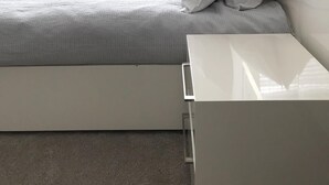 Ett sovrum med en säng, ett sängbord och ett stort fönster.