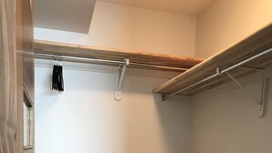 En liten, inredd garderob med heltäckningsmatta, träpaneler och metallstänger för att hänga upp kläder.