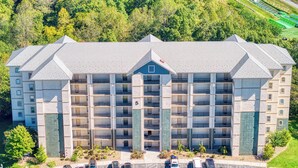 A multi-story hotel with a central entrance, parking lot, and surrounding greenery. - 2 BR and sleeper couch - close to attractions and outlet mall (Pigeon Forge)