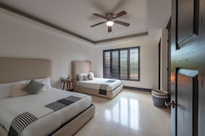 Habitación de hotel con dos camas, un ventilador de techo, una ventana con persianas y una puerta.