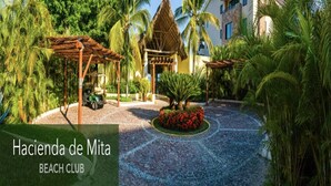 A resort with a beach club, palm trees, a gazebo, and a building with a modern design.