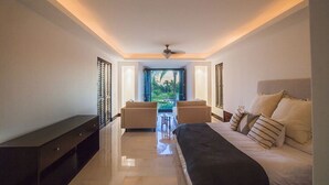 A modern bedroom with a large bed, two sofas, a small table, and a view of greenery through the window.