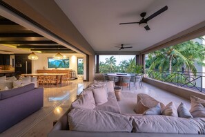 Amplia sala de estar con sofá, mesa de comedor y balcón con vista a palmeras.