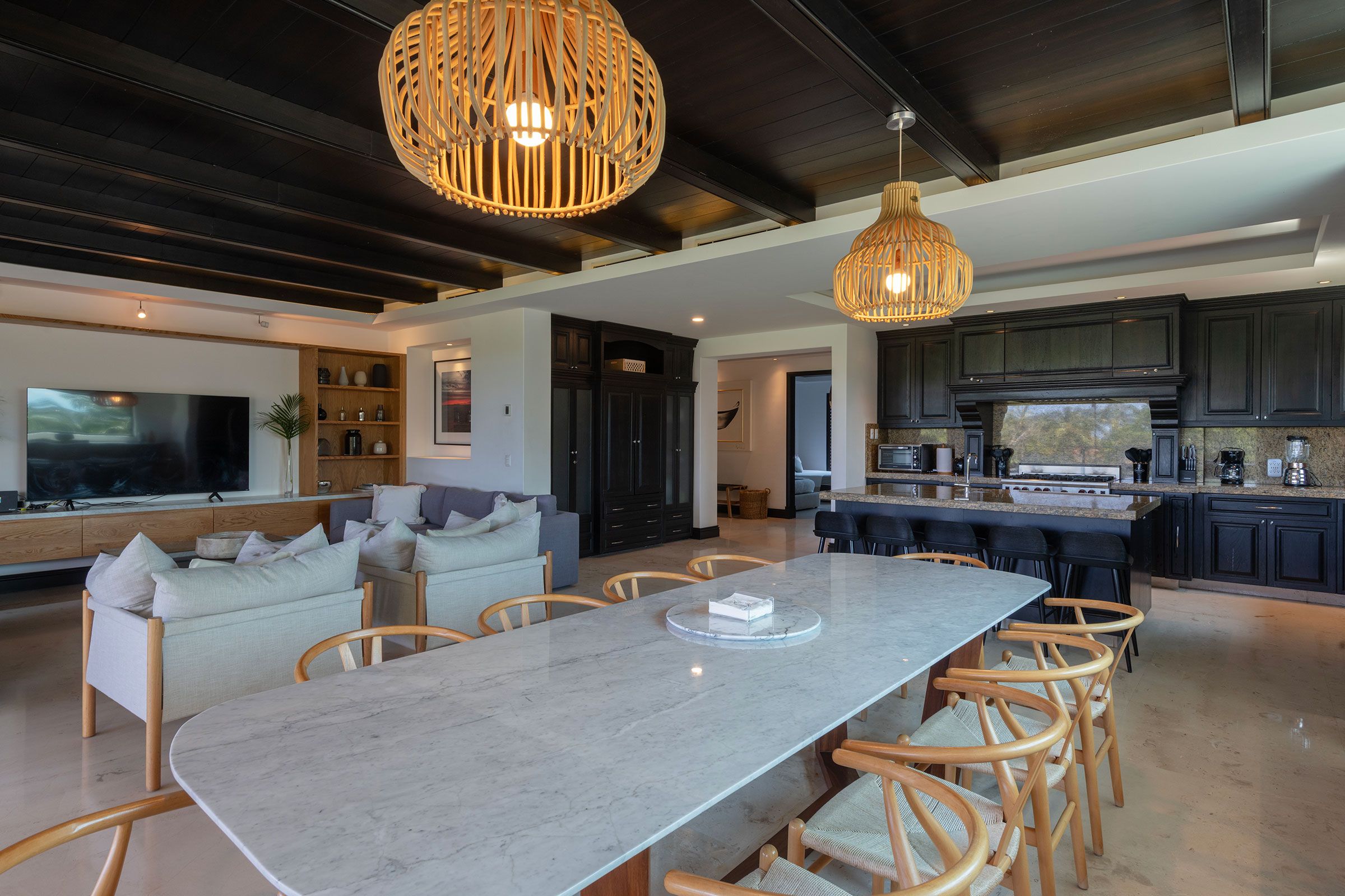 Une cuisine moderne avec des meubles de couleur sombre, un grand îlot central et un coin repas doté d’une table en marbre.
