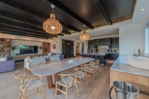 A modern kitchen with dark cabinetry, a central island, and a dining area with a large table and chairs.