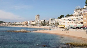 Un paysage urbain côtier avec une plage de sable, de hauts immeubles et un ciel dégagé.