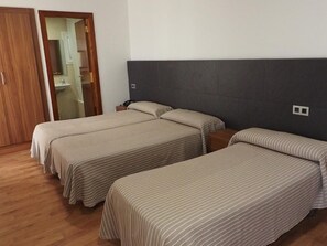 Une chambre d’hôtel avec trois lits, un plancher en bois, une tête de lit sombre et une porte en bois.