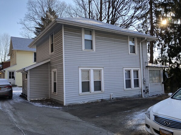 A two-story residential building with a garage, a satellite dish, and a driveway with a parked car. - Baseball Bungalow Retreat (Oneonta)