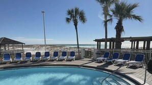 Une piscine bordée de chaises longues et entourée de palmiers, avec vue sur une plage.