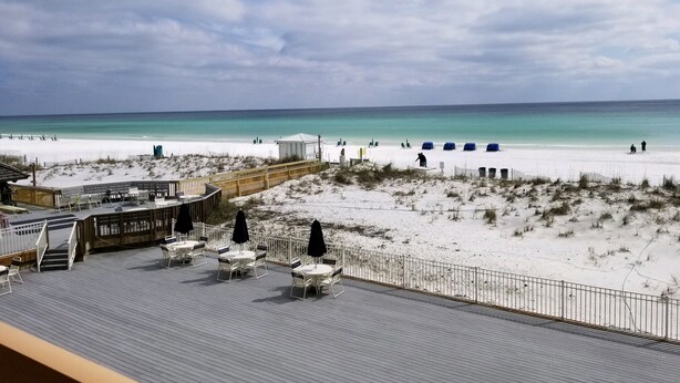 Une vue sur la plage avec une terrasse en bois, des sièges d’extérieur et une zone de plage de sable.