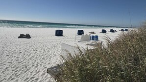 Une plage de sable blanc, un ciel dégagé et plusieurs chaises de plage bleues et blanches.