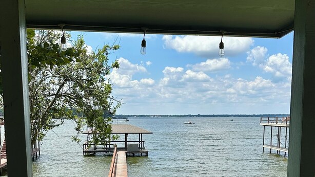 A view from a covered deck overlooking a lake with a dock and a small pavilion.