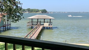 A wooden dock extending into a lake with a covered seating area and a boat in the distance.