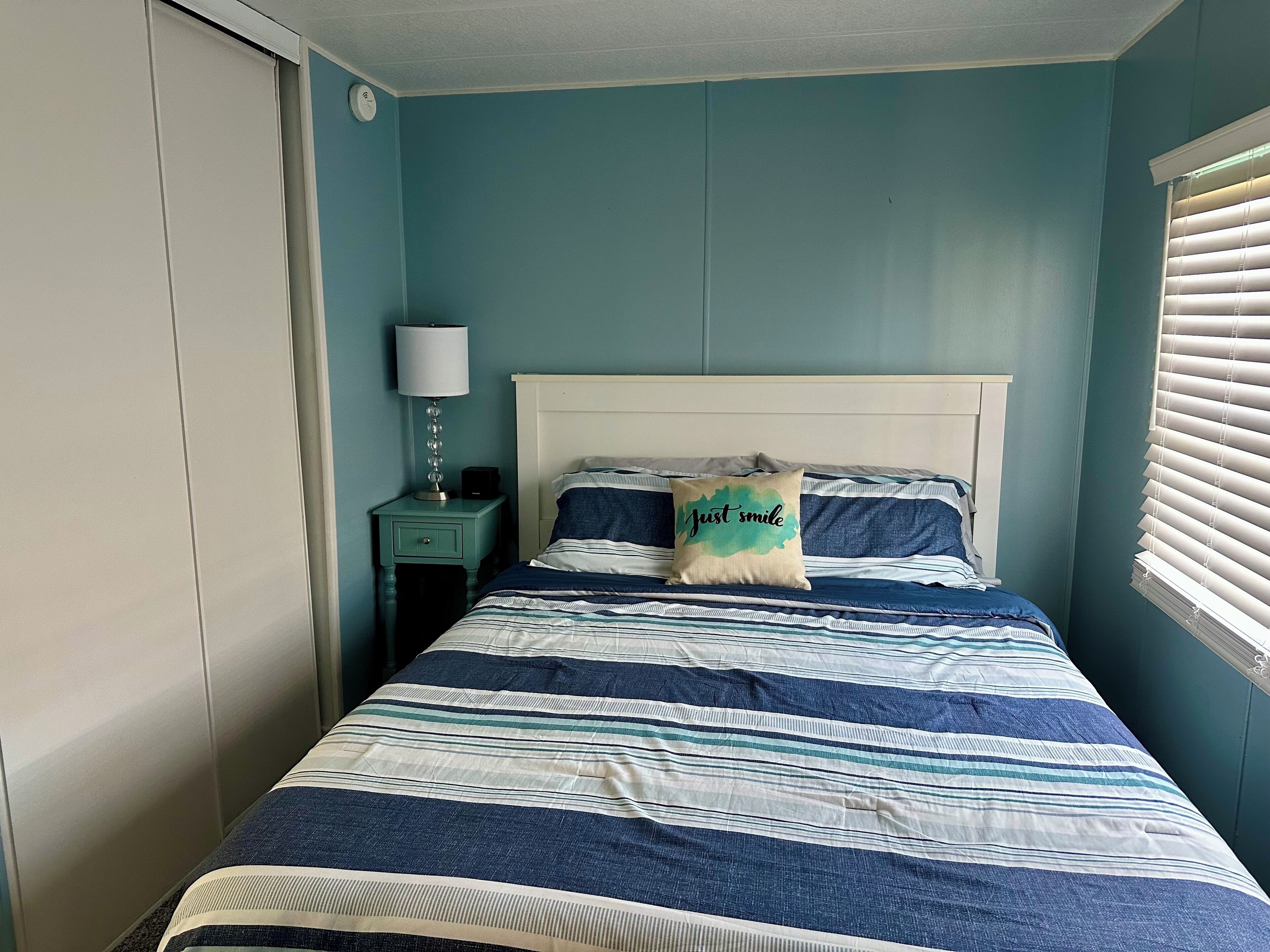 Une chambre à coucher avec un lit, une table de chevet, une lampe et une fenêtre avec des stores.