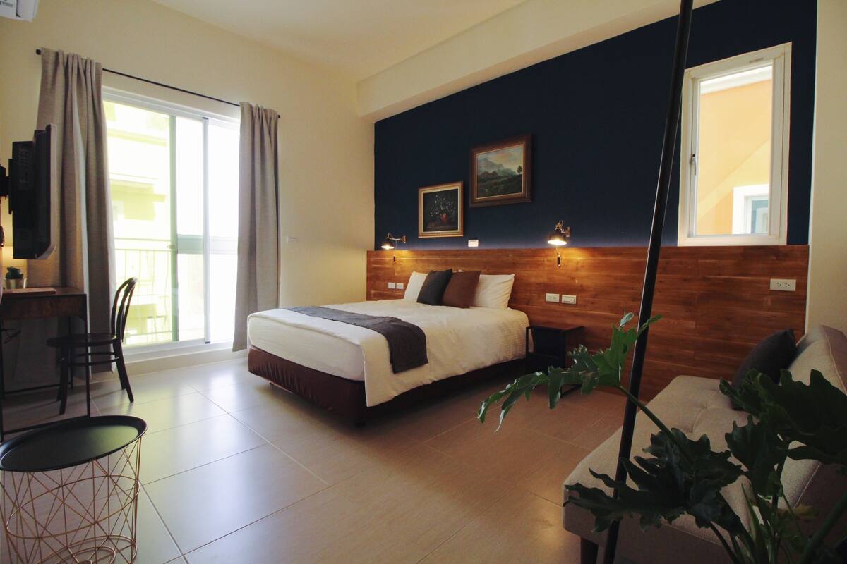 Un dormitorio con cama, escritorio, sillas y un amplio ventanal.