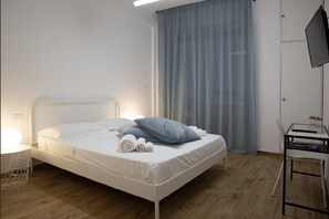 A neatly made bed with pillows and rolled towels, a bedside table with a lamp, and a desk with a computer. - Dora's Room (Pescara)