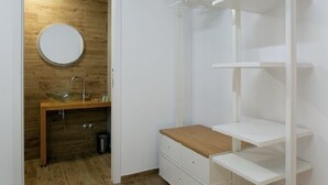 A room with a wooden floor, a round mirror, a glass sink, and white shelving units.