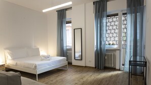 A bedroom with a bed, a bedside table, a chair, a window with curtains, and a radiator.