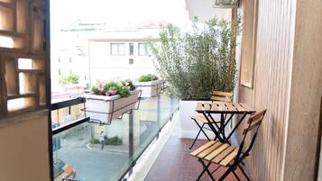 Ein Balkon mit einem Holztisch und Stühlen, Blumentöpfen und Blick auf die Straße darunter.