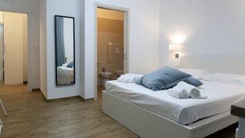 Ein modernes Schlafzimmer mit einem großen Bett, einem Nachttisch, einem Spiegel und einem durch eine offene Tür erreichbaren Badezimmer.