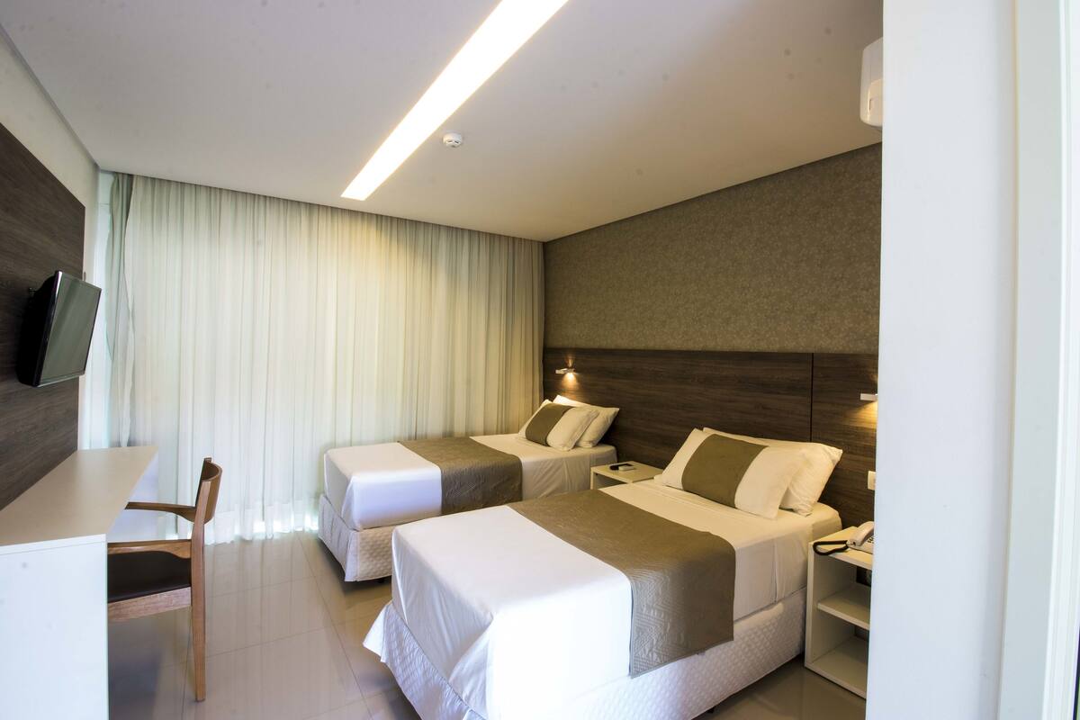 A hotel room with two beds, a desk, a chair, and a television.