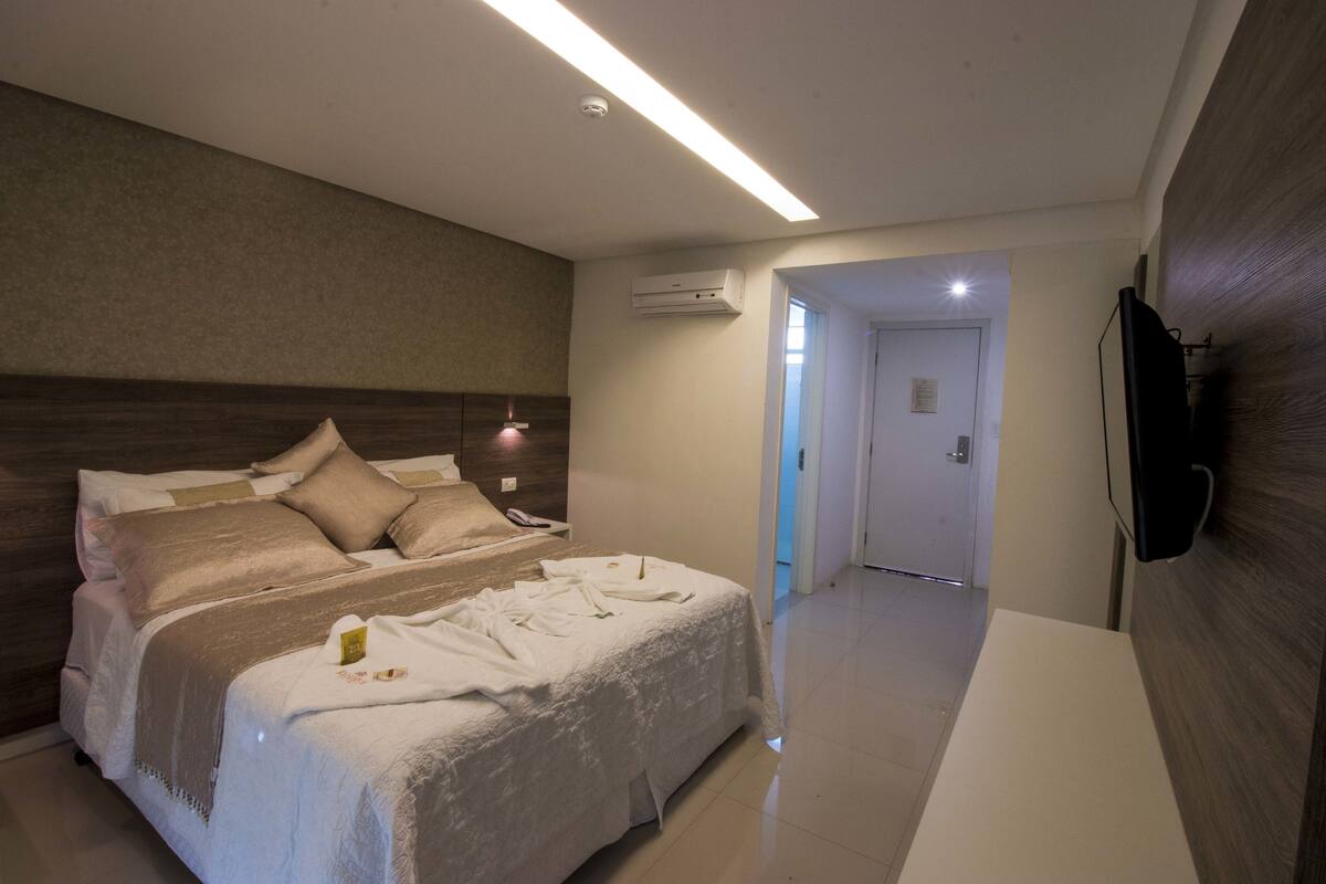 A hotel room with a large bed, a flat-screen TV mounted on the wall, and an air conditioning unit on the wall.