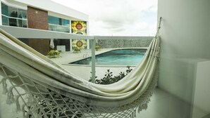 Una hamaca en un balcón con vista a una piscina y un edificio moderno al fondo.