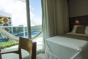 A hotel room with a bed, a chair, a hammock, and a view of a pool and building with colorful patterns. - Reserve Hotel Surubim (Surubim)