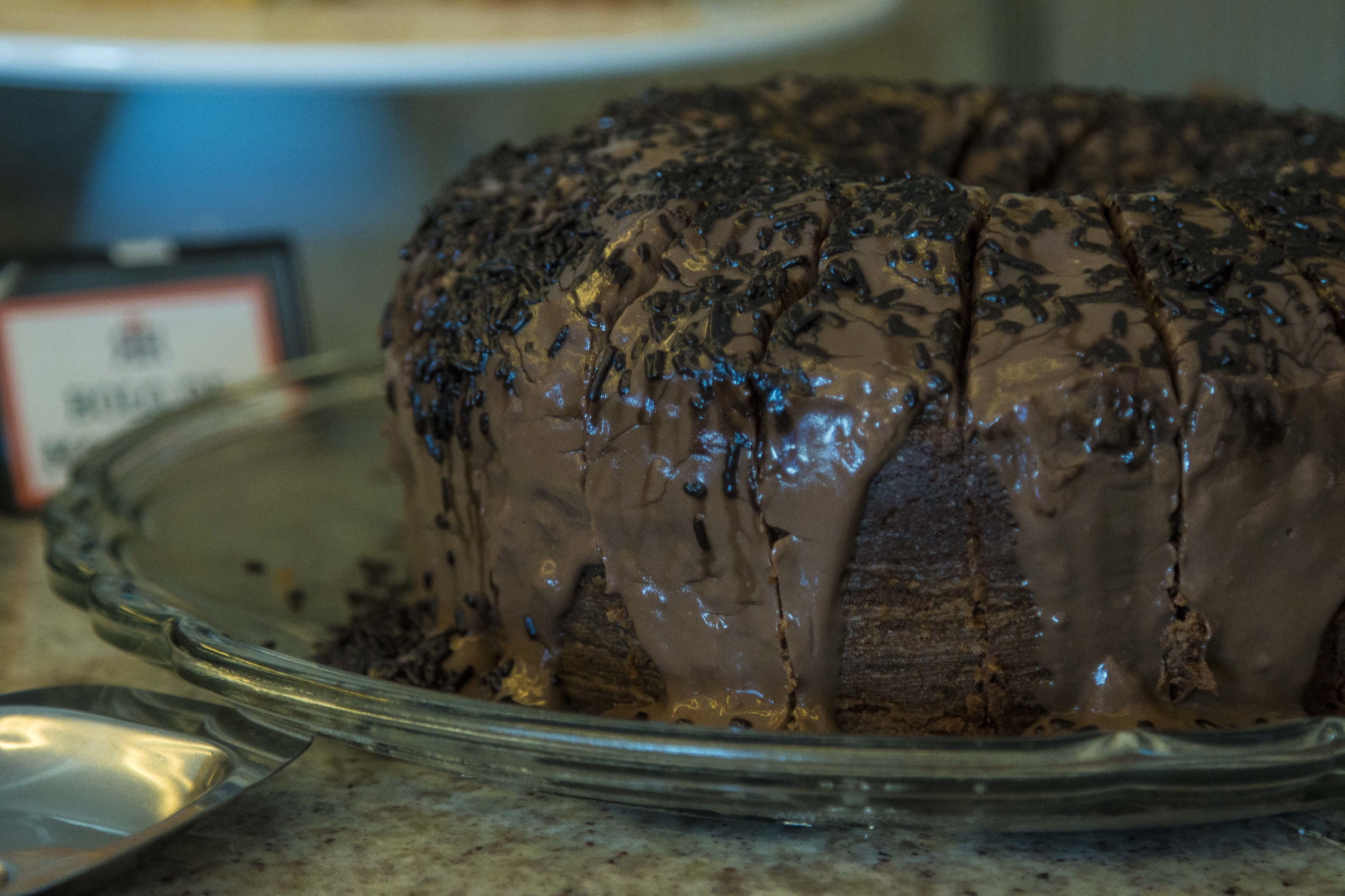 A chocolate cake with chocolate shavings on top, placed on a glass cake stand.