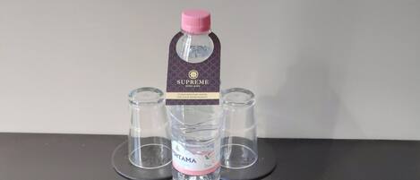 Uma garrafa de água com o rótulo "Supreme Hotel & Spa", uma etiqueta, três copos vazios e um livreto roxo intitulado "Minibar".