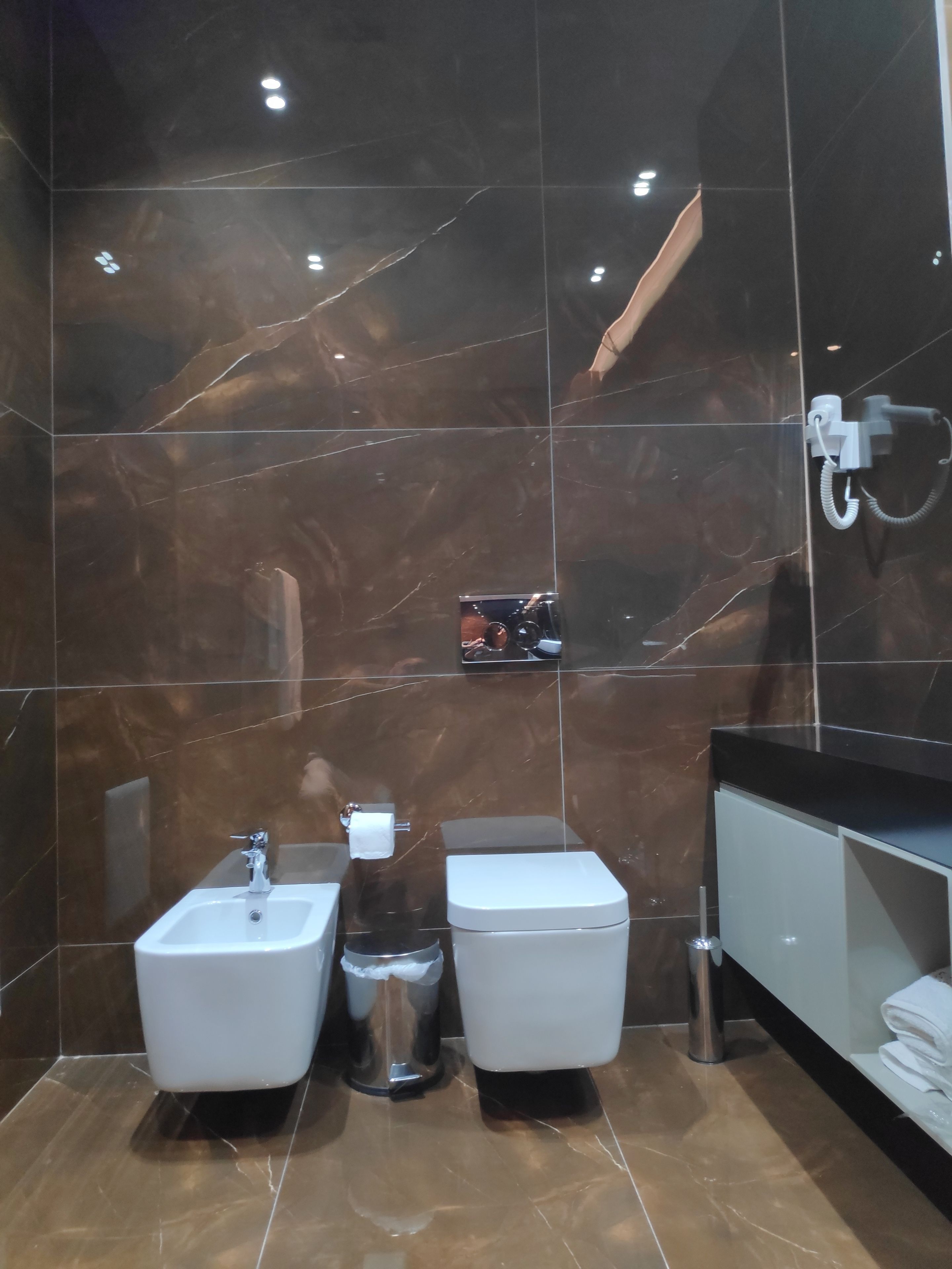 A modern bathroom with dark marble walls, a white sink, a toilet, and a shower area.