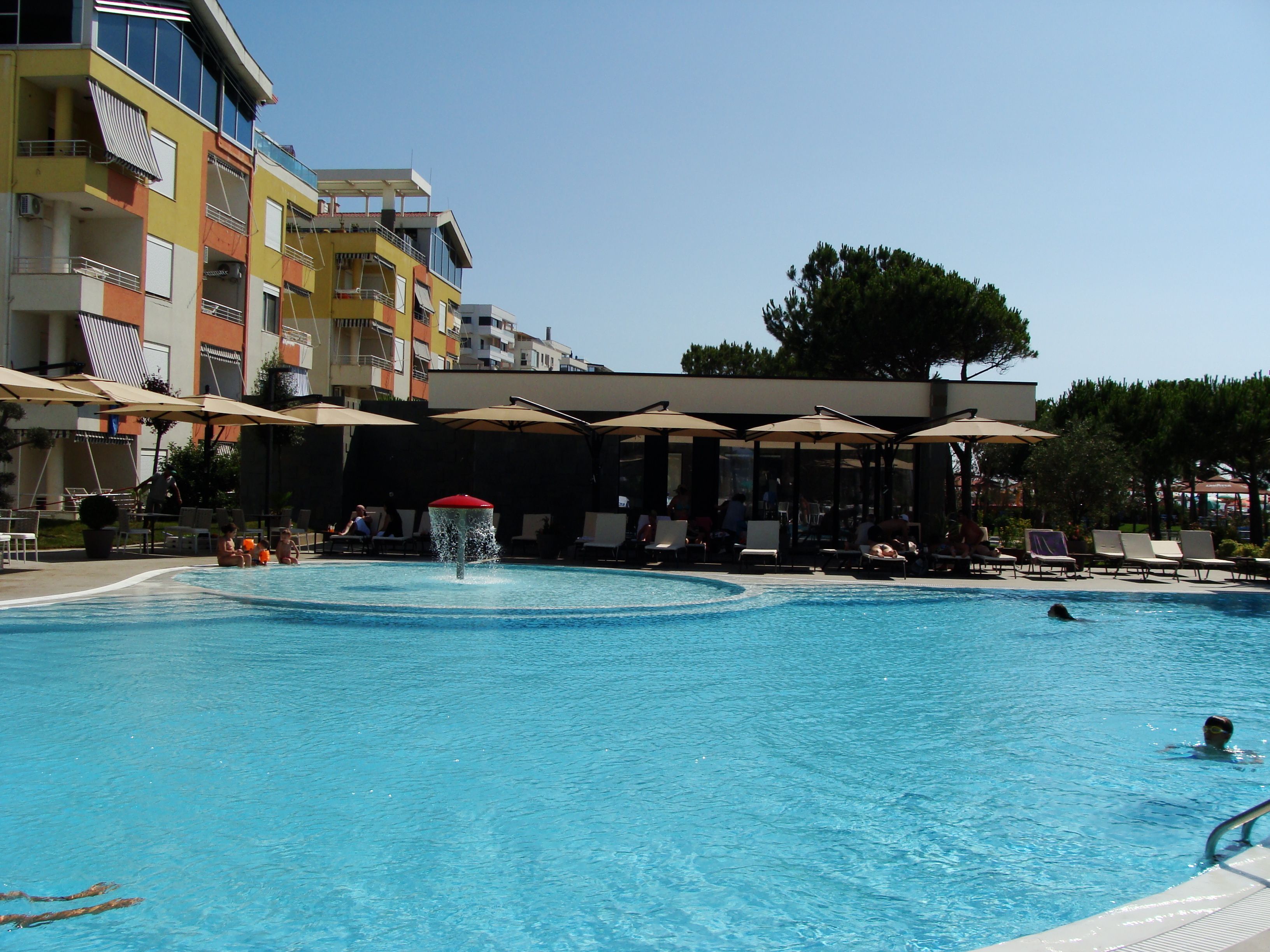 A swimming pool with lounge chairs and umbrellas, surrounded by multi-story buildings.