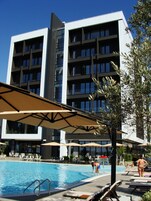 Un hotel moderno con zona de piscina, incluyendo sillones de descanso y sombrillas.