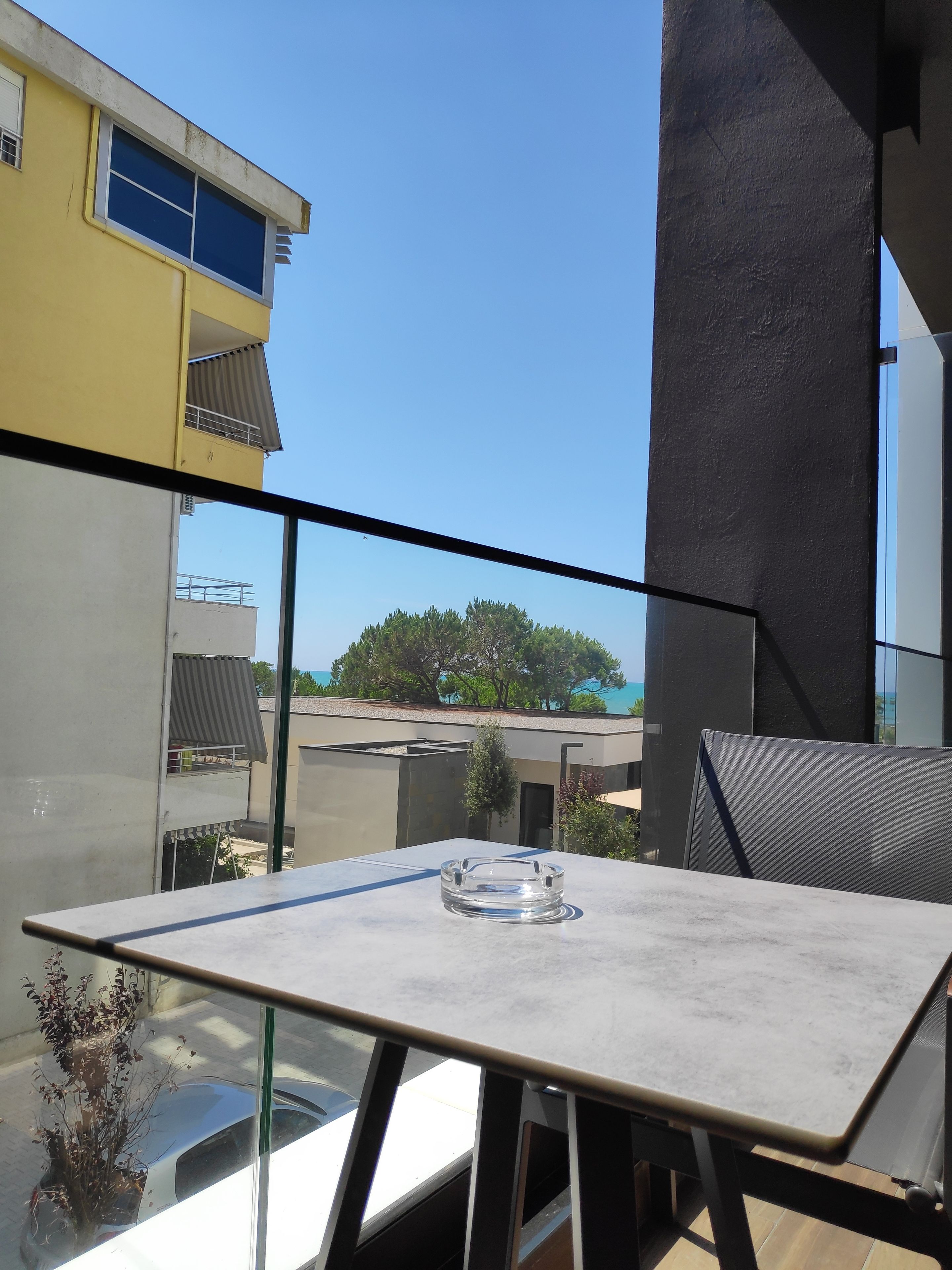 A balcony with a table and chairs, overlooking a building and trees.