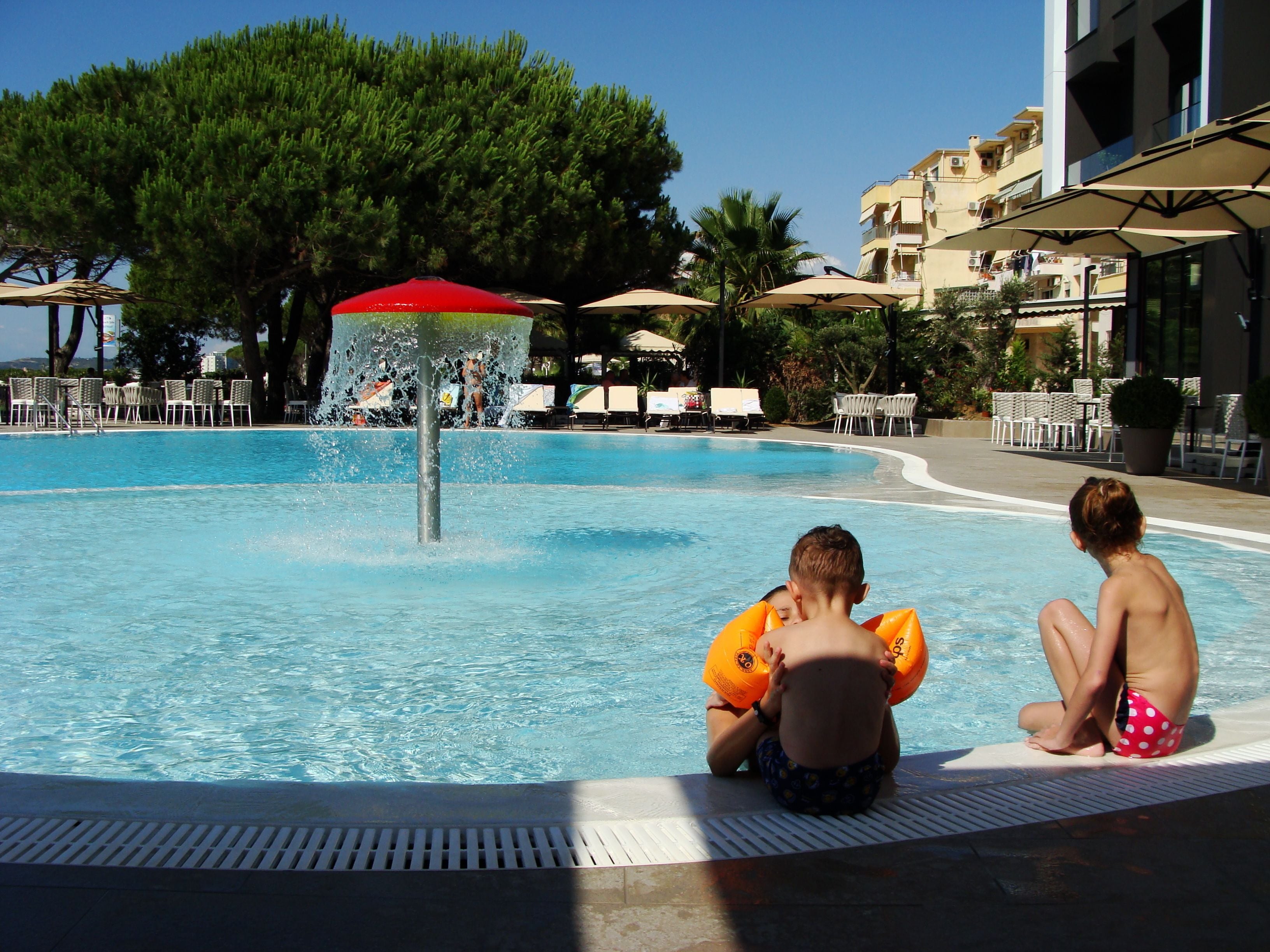 Una piscina con fuente de agua, sillas de descanso y sombrillas.