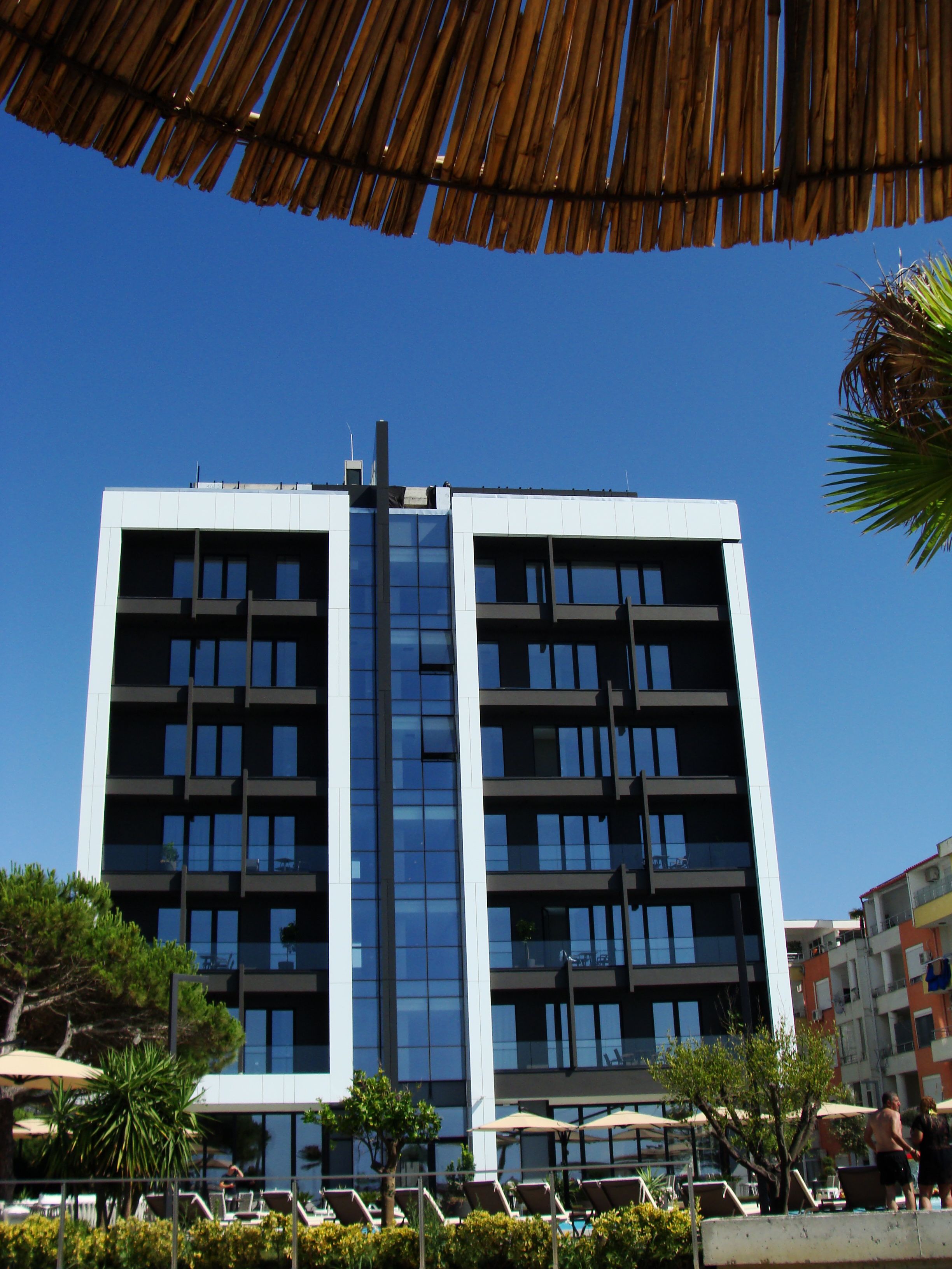 Um edifício moderno de vários andares, com fachada de vidro central, rodeado por áreas verdes e espaços para sentar ao ar livre.