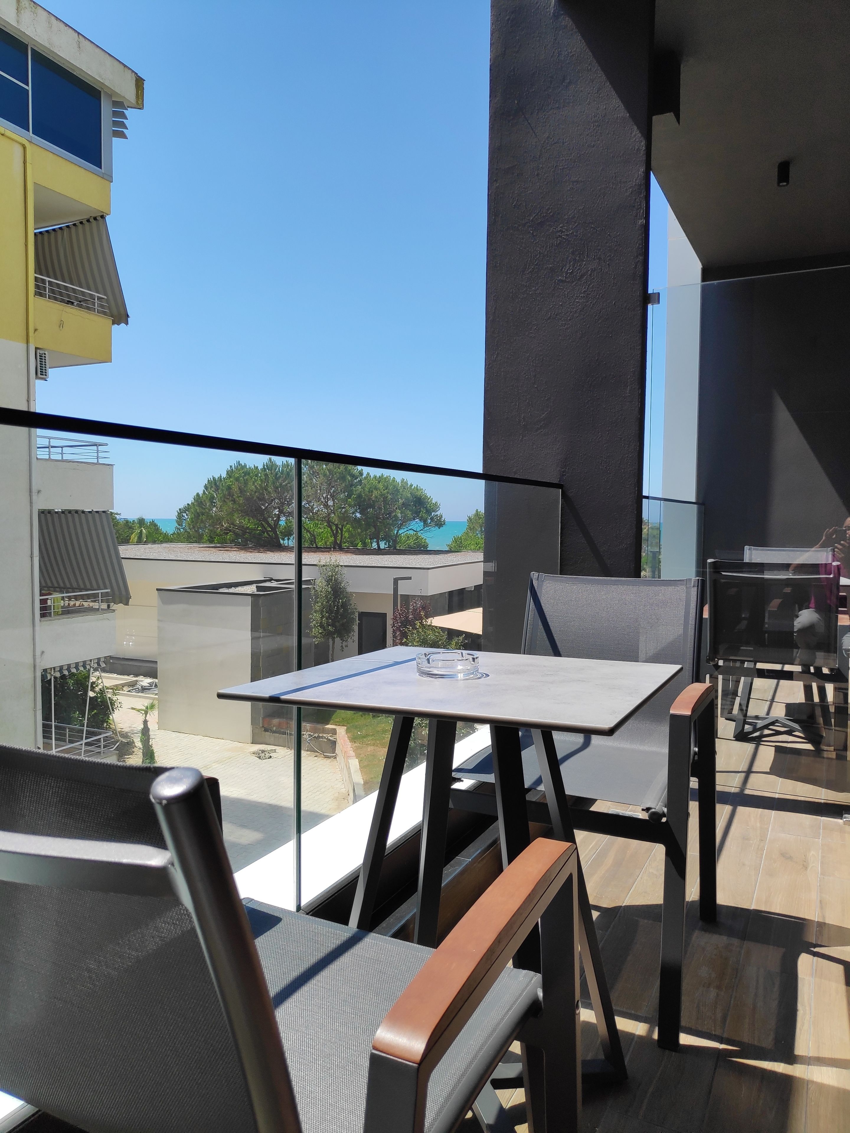 Un balcón con mesa y sillas, con vista a un edificio y un cielo despejado.